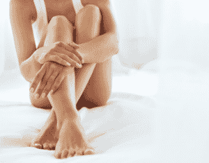 A woman is sitting on a white blanket with her arms around her legs