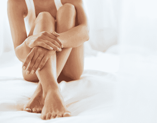 A woman is sitting on a white blanket with her arms around her legs