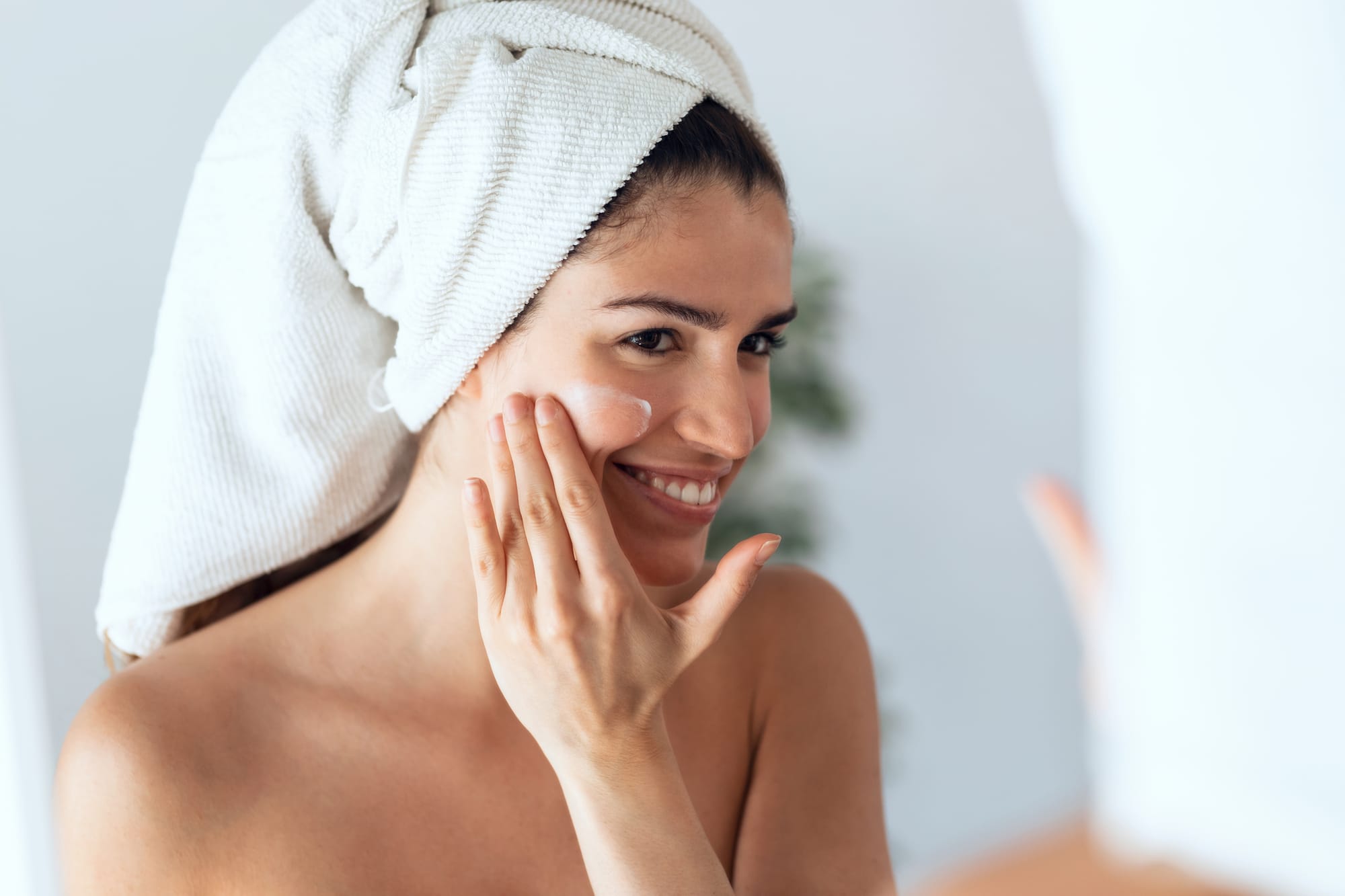 Beautiful young woman caring of her skin while putting on cream