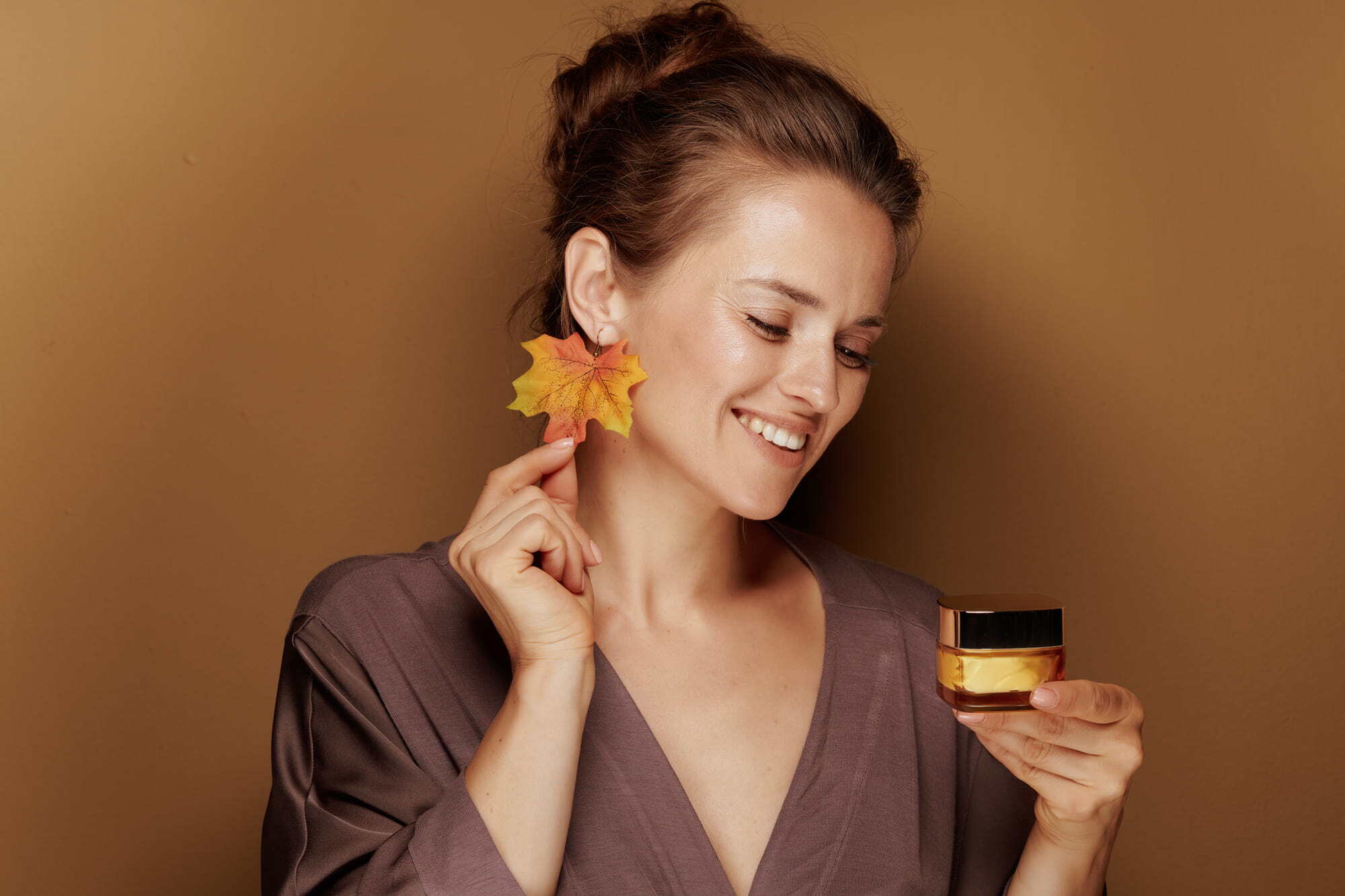woman with radiant skin sat against fall-themed background holding a skincare product