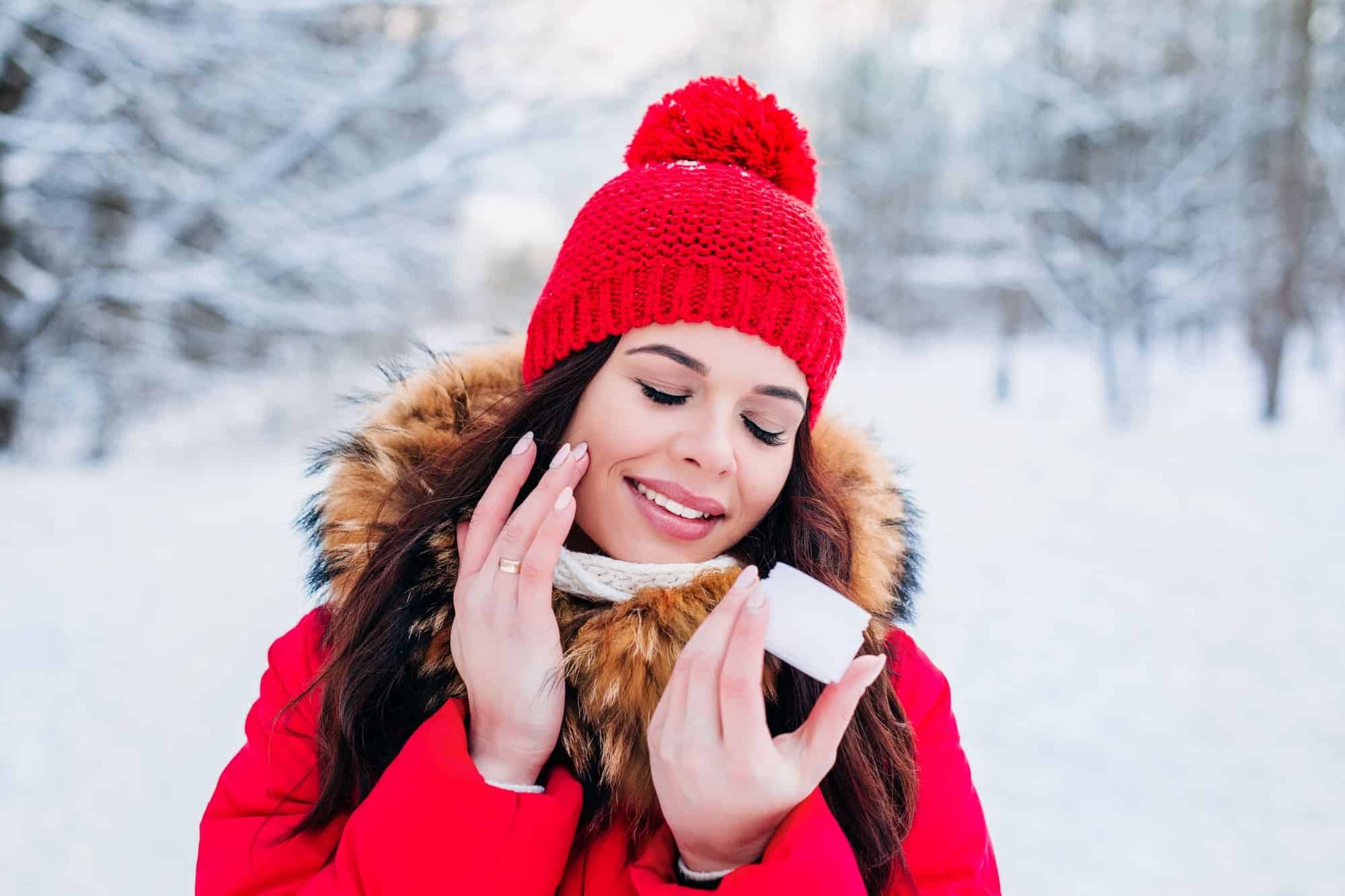 young woman in red winter coat enjoying a skin care product