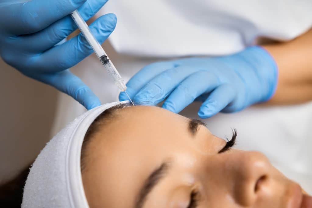 Close up of beautician hands injecting botox in female forehead.
