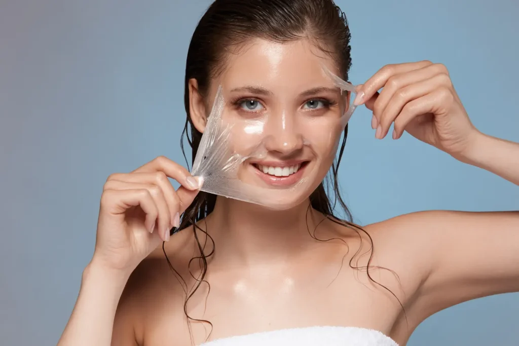 A happy woman gently removes a face peel mask, revealing radiant, healthy skin underneath. Skincare beauty routine.
