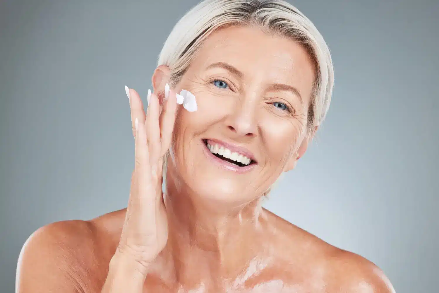 Smiling senior woman applies skin peeling treatment to her face. 