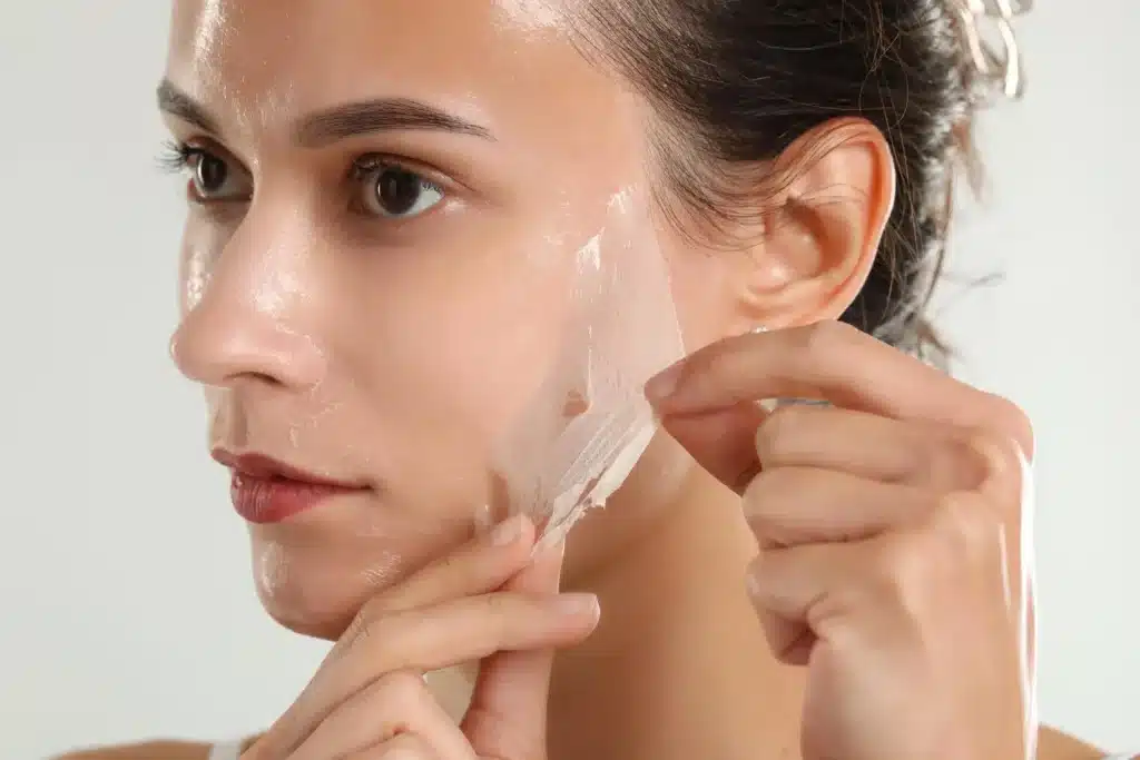 A woman gently peels off a face mask, revealing fresh, smooth, radiant skin underneath.