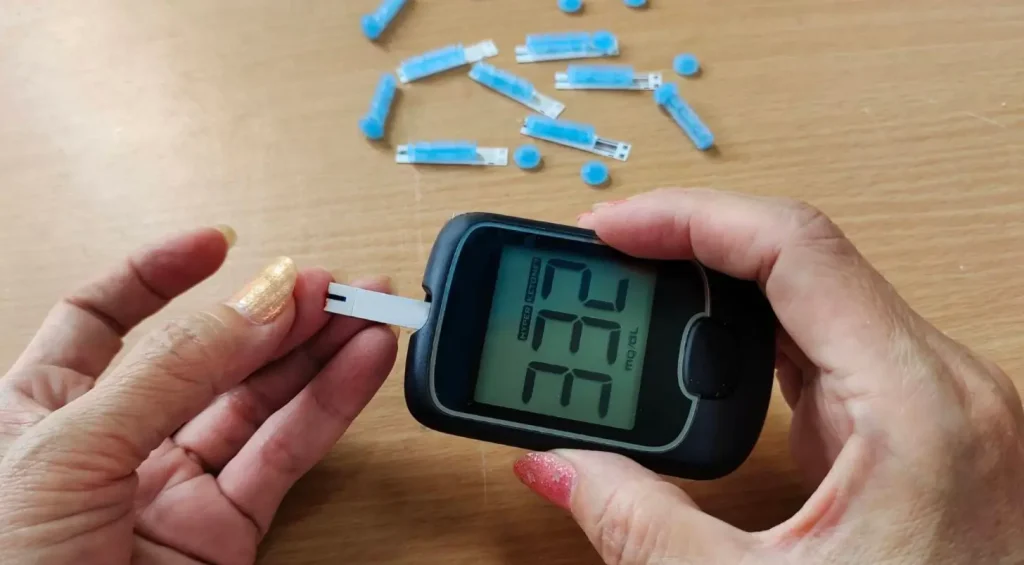 Person using a glucometer to check blood sugar levels, with lancets scattered, for diabetes management.
