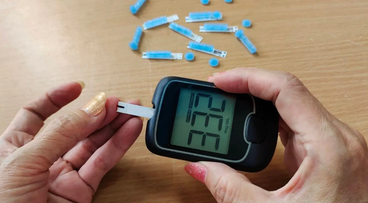 Person using a glucometer to check blood sugar levels, with lancets scattered, for diabetes management.