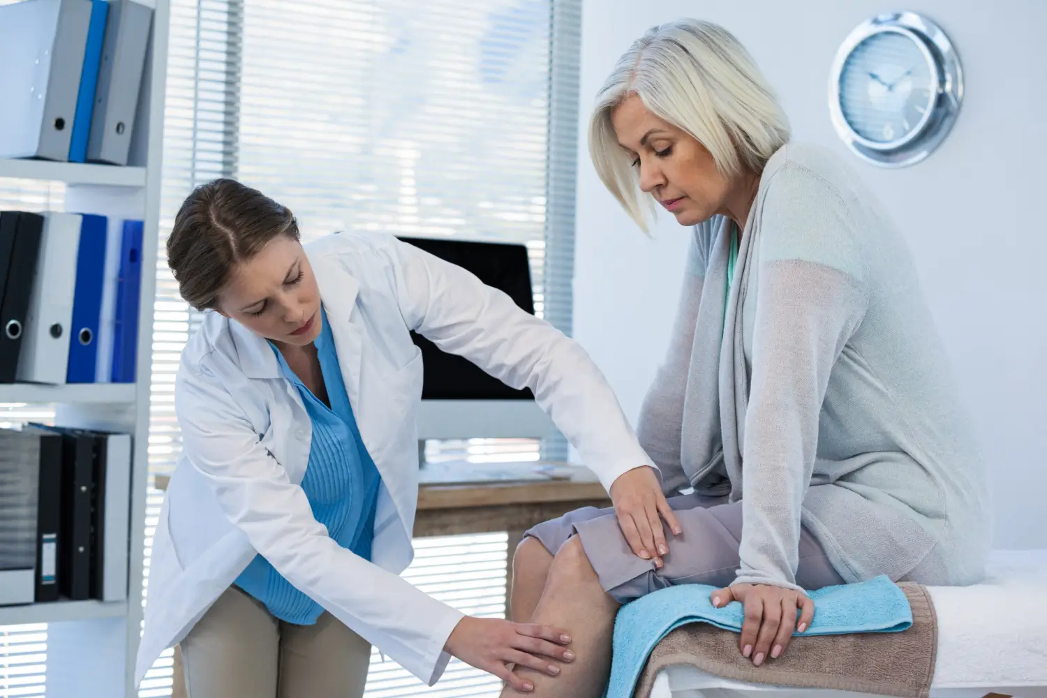 Caring doctor examines senior patient's knee.