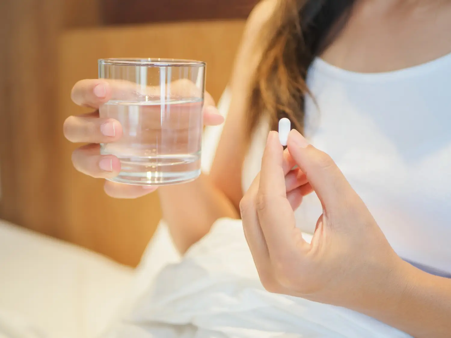 Woman holds a capsule medicine on one hand and a glass of water on the other.