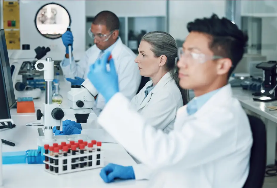 Three scientists in lab coats and gloves work at a laboratory bench with test KPV Peptide focusing on experiments and analysis in a bright, modern research environment.